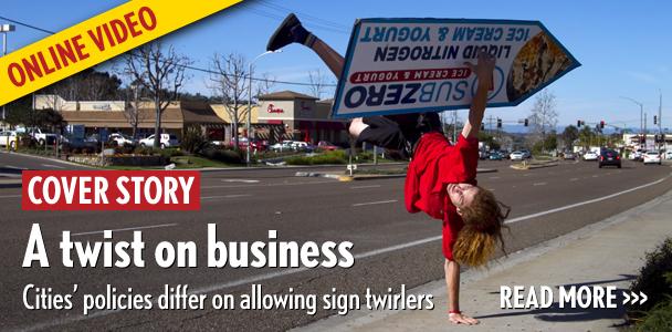 John Murray catches his sign while standing on one hand along El Camino Real near Encinitas Boulevard on Feb. 16. Murray has been spinning signs on and off for six years.